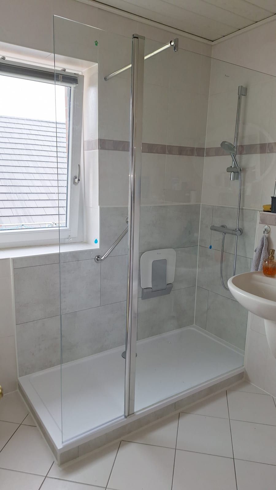 Nachher: Dusche mit Glaswand, Klappsitz und Thermostat-Armatur unter dem Fenster