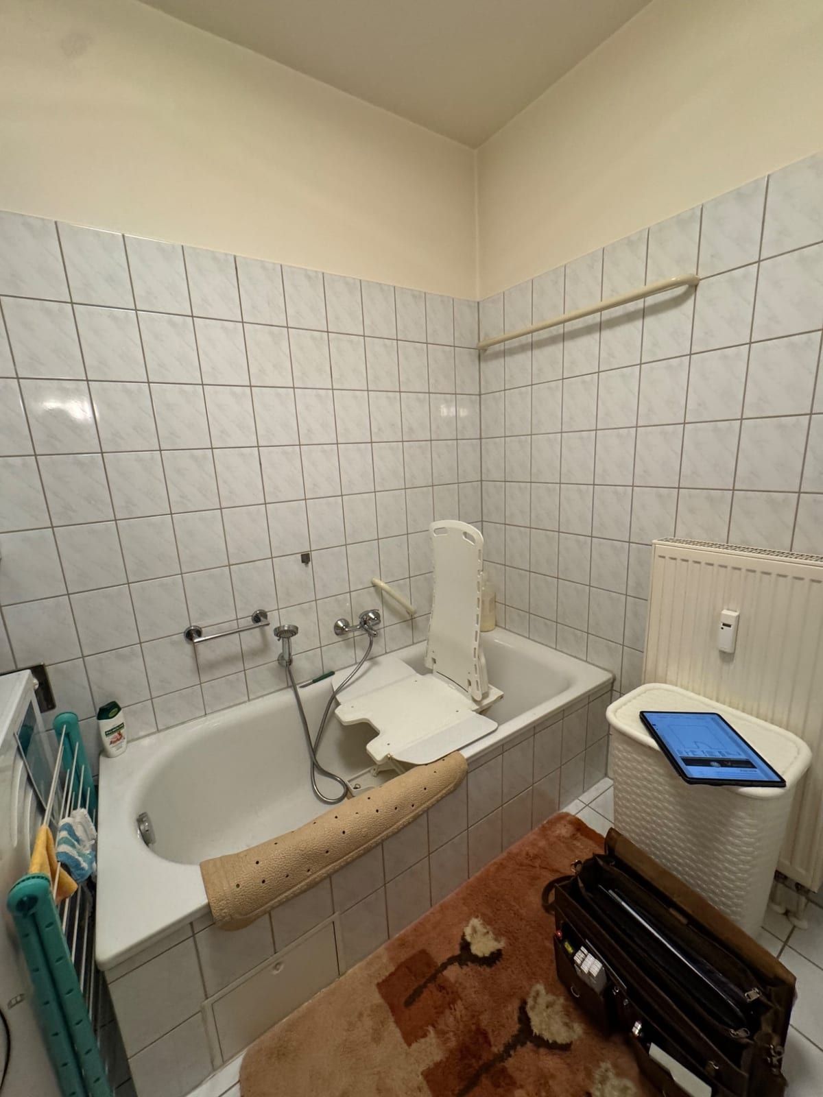 Vorher: Badewanne mit Badewannenlift in einem weiß gefliesten Bad