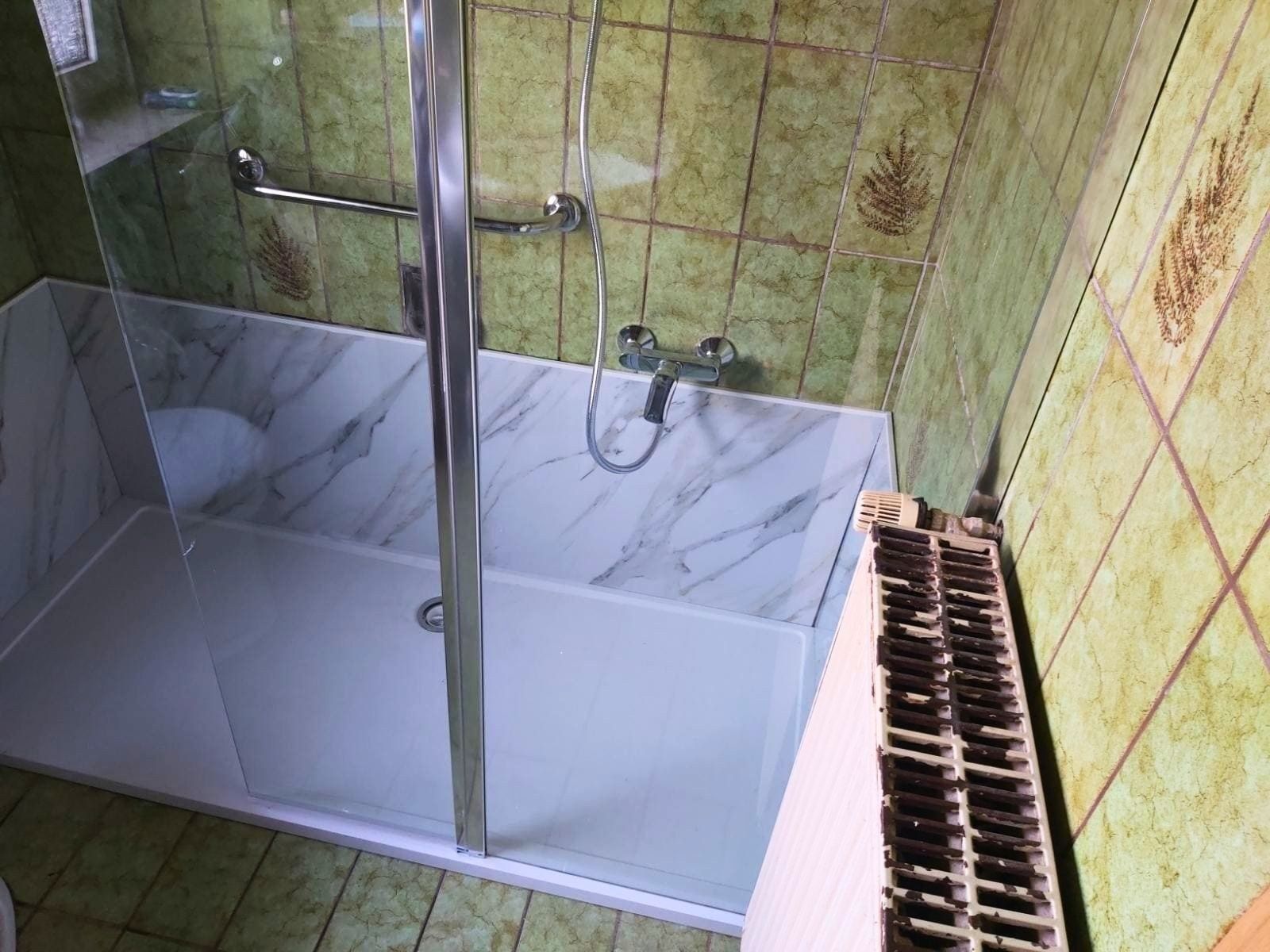 Fertige Dusche mit Glaswand, hellen Wandpaneelen und Haltegriff